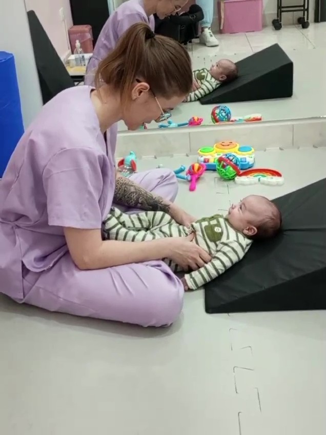 Fisioterapeuta posicionando bebê sobre cunha durante atendimento no Neuro Acolher